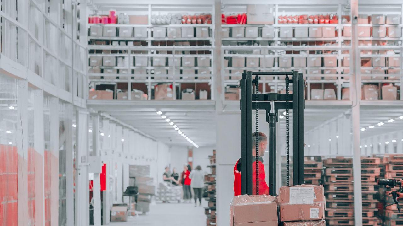 man in black pants and black jacket standing on black and red fork lift